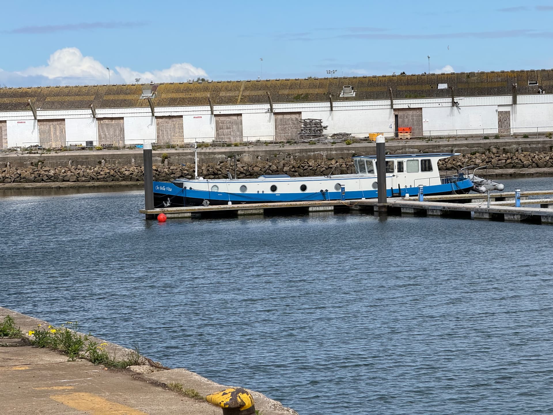 Che Bella Vita moored bow-on to a marina pontoon with a long warehouse behind