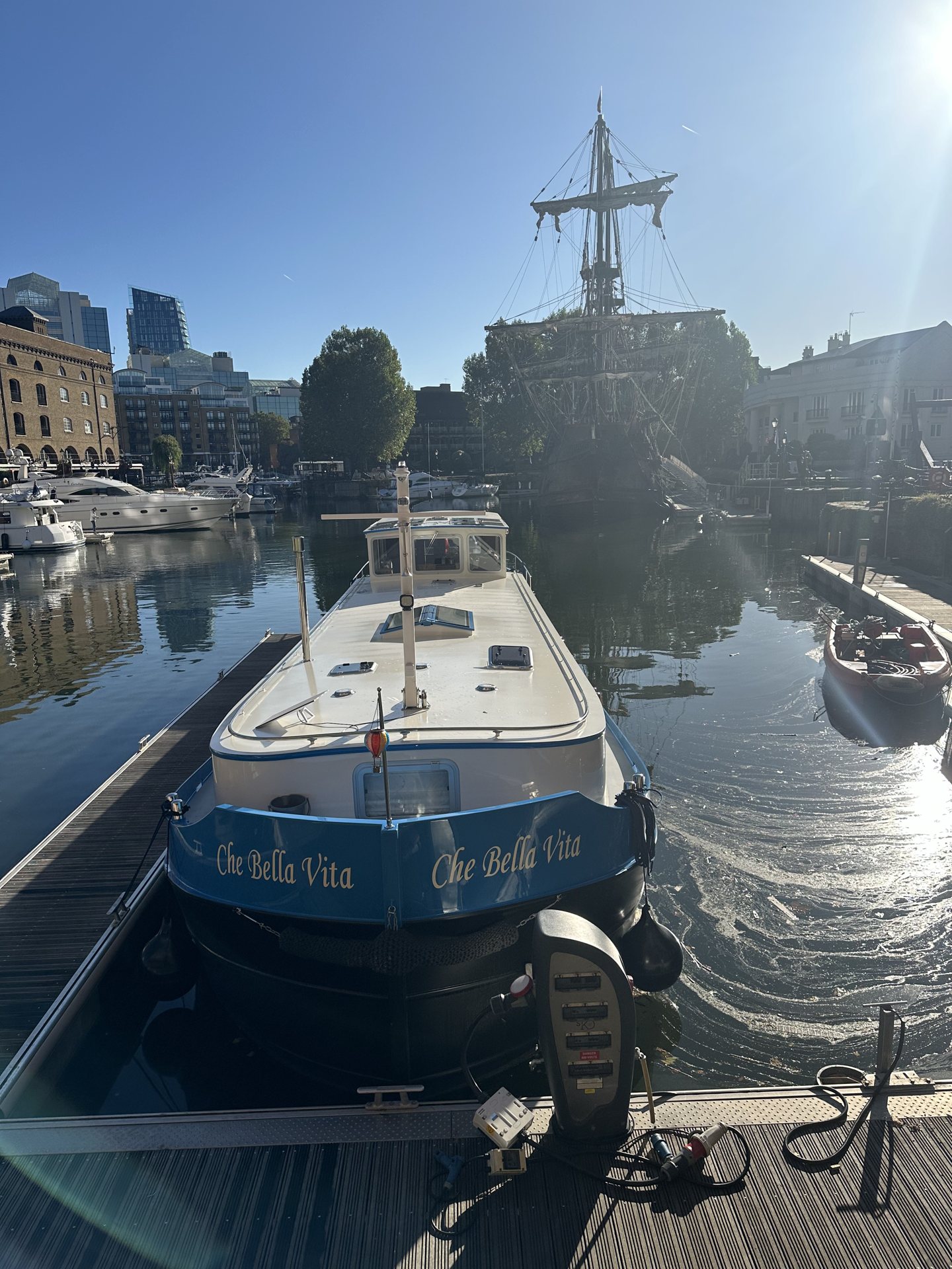 Che Bella Vita bow-on in sunshine at St Katharine Docks with a tall ship behind