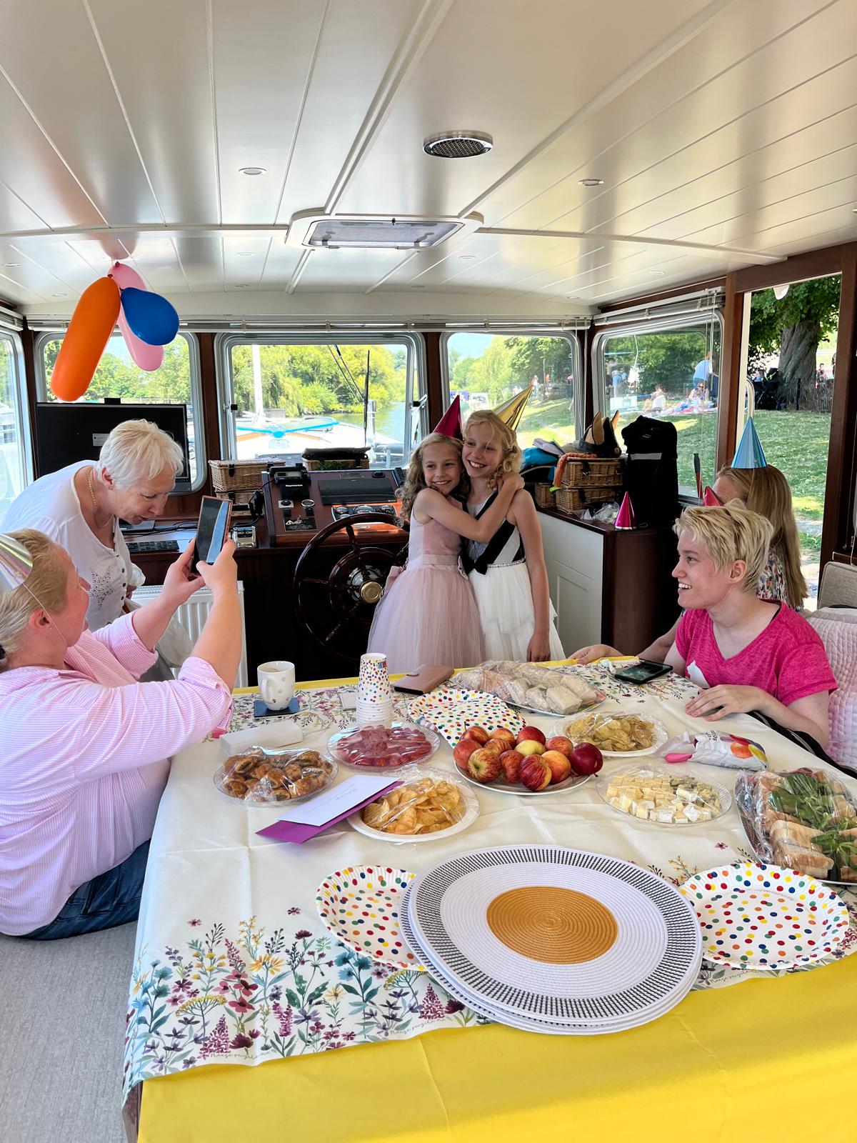 Two young girls hugging at Che Bella Vita's steering wheel, balloons and a party table behind them