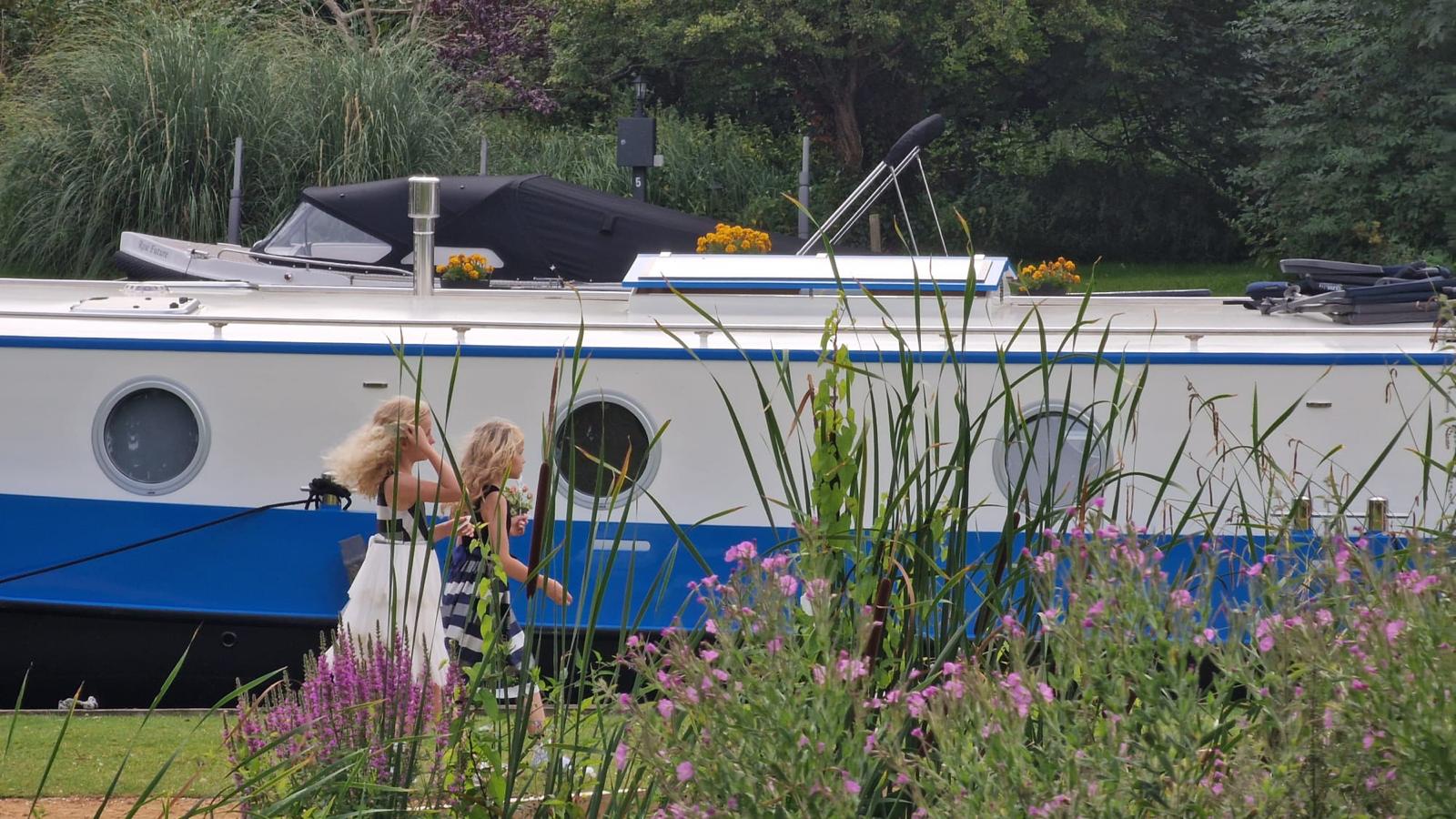 Two young girls walking along the towpath past Che Bella Vita, moored among reeds and wildflowers